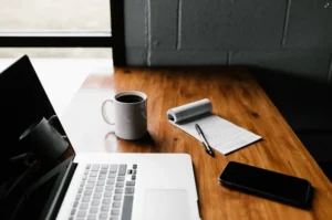 Modern workspace with laptop, coffee cup, notepad, pen, and smartphone on a wooden desk, representing office work, productivity, remote working, and professional planning